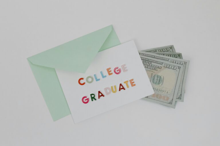 A college graduation card with dollar bills in a mint green envelope on a white surface.